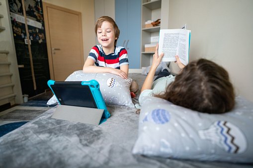 Children using technology and reading a book at home