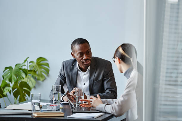 African American Executive in Meeting Portrait of young black businessman talking to female colleague during meeting in office against pale blue wall, copy space bossy stock pictures, royalty-free photos & images