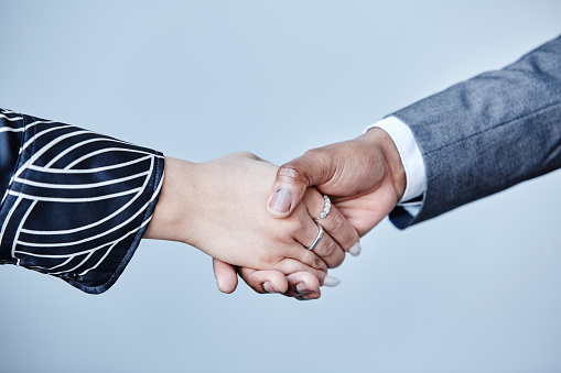 Minimal closeup of two business partners shaking hands against grey background