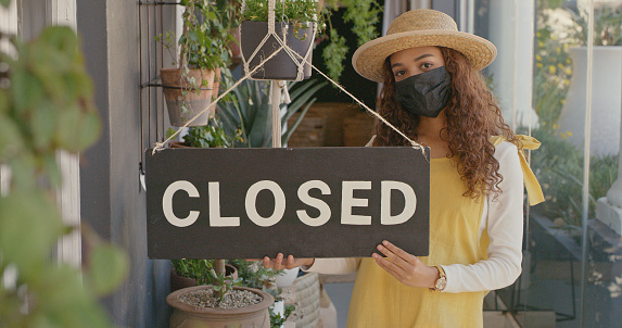Young female florist holding a closed sign while wearing a mask at work