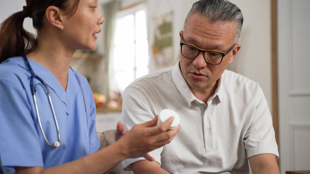 primer plano de un anciano asiático escuchando con concentración mientras la enfermera le da la píldora recetada y le dice cómo usarla en casa. - prescription plan fotografías e imágenes de stock