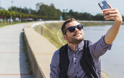 Mid adult man in sunglasses using mobile phone outdoors near the river.