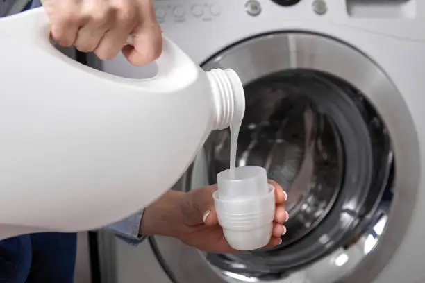 Photo of Girl in T-shirt carefully pours transparent conditioner for flattening laundry