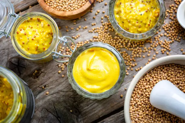 Different types of mustard and mustard seeds on a rustic wooden board