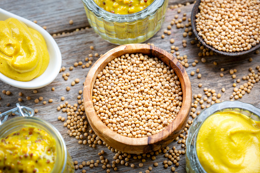 Different types of mustard and mustard seeds on a rustic wooden board