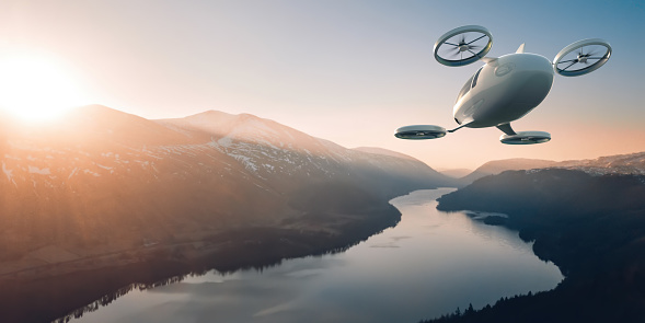 A generic electric vertical take off and landing aircraft flying high off the ground through a valley over a wide river with mountains of either side as the sun is just rising / setting. The eVTOL is white and has two front and two rear rotors.