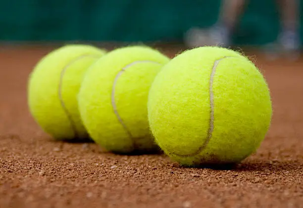 three yellow tennis balls on a read court, right end ball in focus.