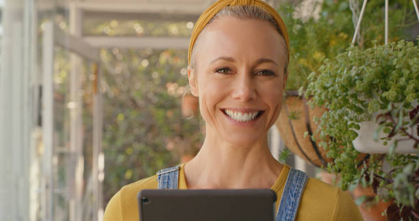 istock Mature caucasian female florist smiling while using a digital tablet at a nursery 1395336396