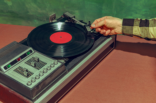 Image of old-fashioned vintage vinyl record player isolated over dark green background. Retro music. Revealing past memories. Concept of pop art, fashion, music, mix old and modernity