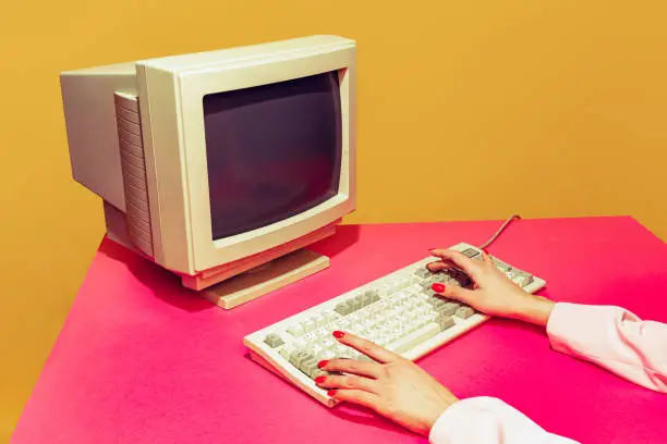 Colorful image of vintage computer monitor and keyboard on bright pink tablecloth over yellow background. Typing information. Concept of retro pop art, vintage things, mix old and modernity