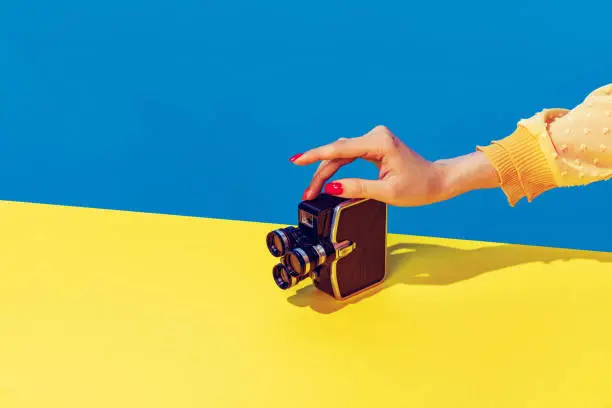 Photo of Pop art photography. Colorful image of retro photo camera on bright yellow tablecloth isolated over blue background