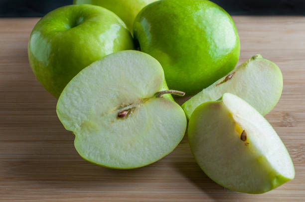 Green apples on a wooden cutting board with a black background side view, concept of healthy food macro photography