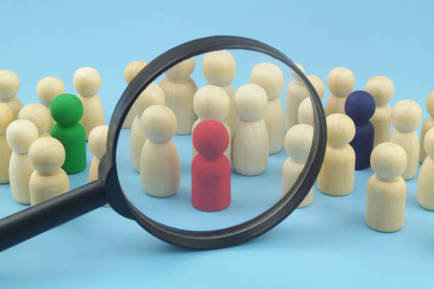 istock Group wooden people figures with few colored figures under magnifying glass on blue background. 1395340258
