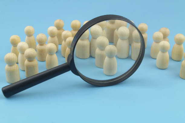 istock Many wooden figures and magnifying glass on blue background. 1395340282