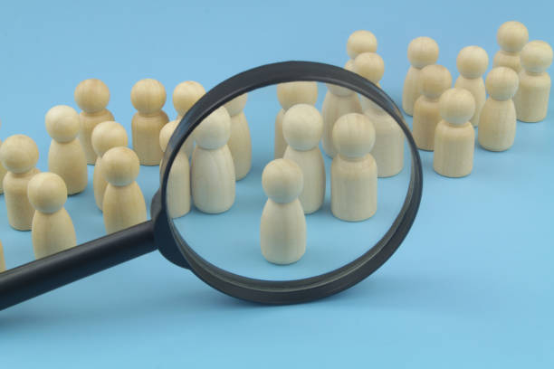 istock Many wooden figures and magnifying glass on blue background. 1395341054