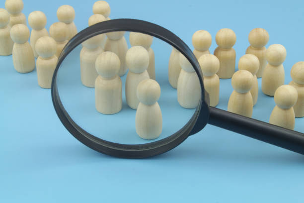 istock Many wooden figures and magnifying glass on blue background. 1395341059