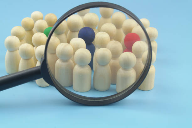 Group of not colored figures with few colored under magnifying glass on blue background. stock photo