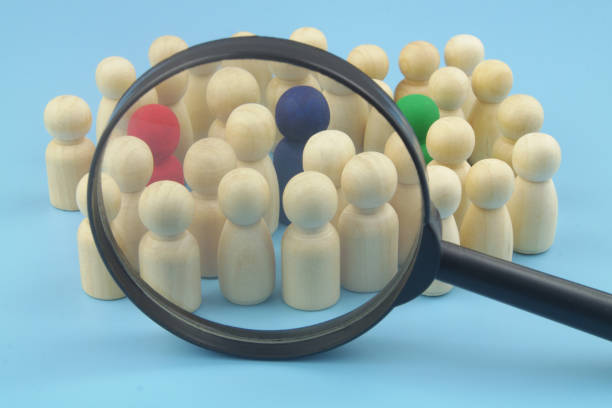 istock Group of not colored figures with few colored under magnifying glass on blue background. 1395341269