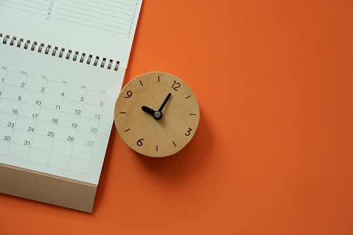 close up of calendar and clock on the orange table background, planning for business meeting or travel planning concept