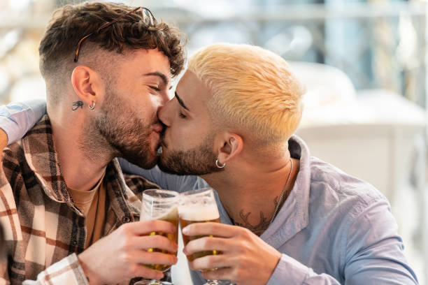 casal gay da moda em um encontro, passando um tempo juntos, beijando, bebendo cerveja. estilo de vida de pessoas reais. amor. - gay man homosexual men kissing - fotografias e filmes do acervo