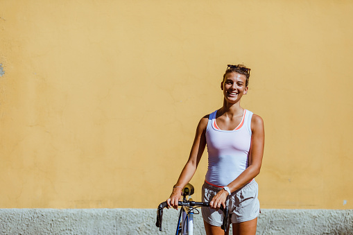 Portrait of happy woman with bike, yellow wall in the background