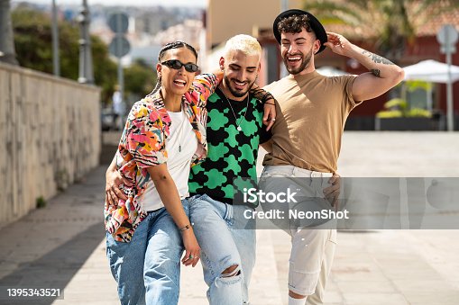 istock Three happy young people walking in the city, talking to each other, laughing and having fun. Multiethnic group of friends. 1395343521
