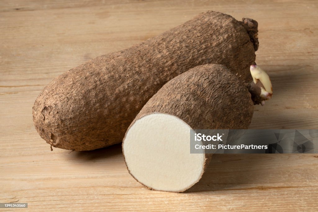 Whole and halved raw African yam on wooden background Whole and halved raw African yam on wooden background close up Yam Stock Photo