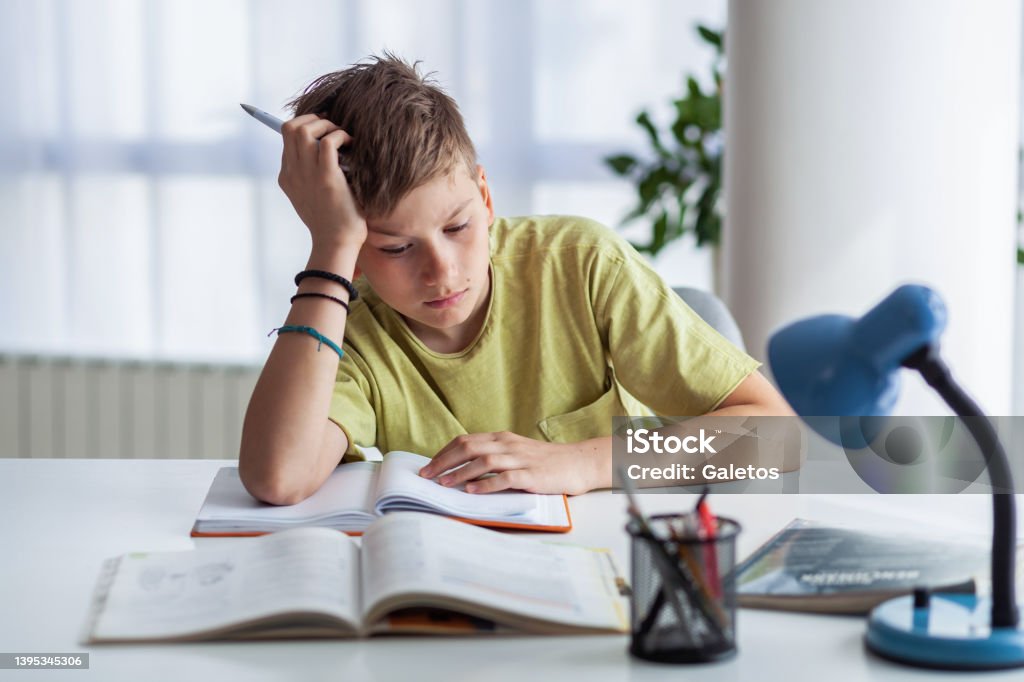 Ugh, I'm so bored with this homework! Bored elementary student feeling tired while reading a lecture at home. Textbook Stock Photo