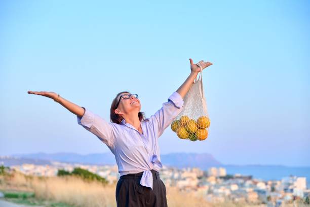 feliz mulher alegre com as mãos levantadas com grade de laranjas, fundo do céu azul - arms raised people orange blue - fotografias e filmes do acervo