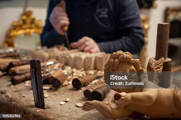 Master Woodcarver At Work Wood Shavings Gouges And Chisels On The Workbench Angel Wood Carved In The Foreground Stock Photo - Download Image Now