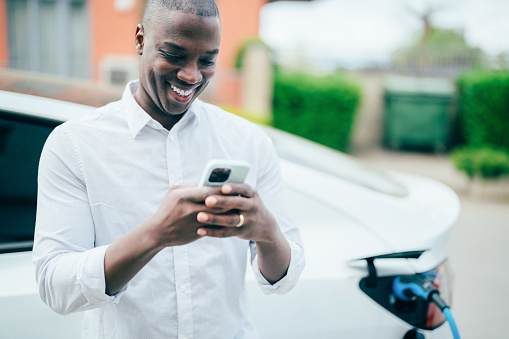 Man texting on phone while charging electric car