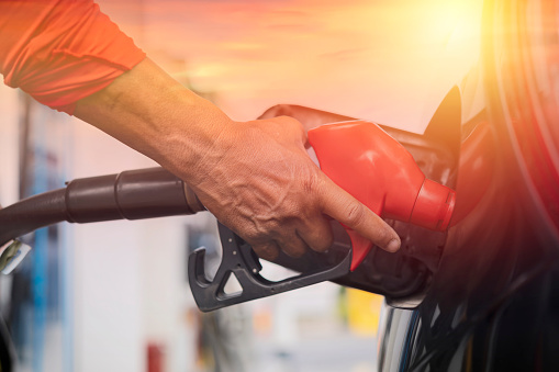 Man Handle pumping gasoline fuel nozzle to refuel. Vehicle fueling facility at petrol station. White car at gas station being filled with fuel. Transportation and ownership concept.