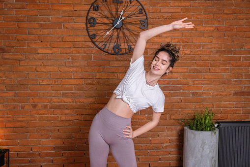 Active and healthy young Caucasian woman stretching her body, during homeworkout in her modern and cozy home