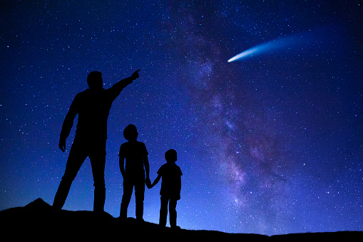 Silhouette of father with two boys on the night of Milky Way, looking at the sky surprised by unexpected comet.