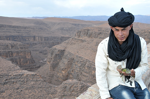 Souss-Massa-Draa, Morocco - March 19, 2012: Young man with an iguana in the Moroccan Atlas Mountains