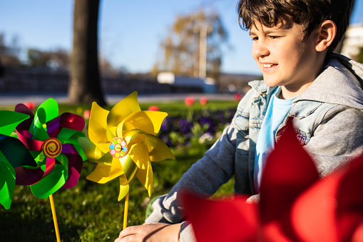 A cute boy is making a windfarm by sticking toy windmills into the ground on a sunny spring day