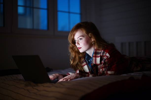 istock Young woman working on laptop while laying in bed at night 1395364190