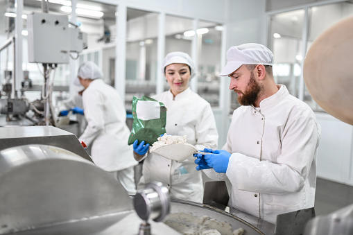 Bearded Male Worker In Food Processing Plant Using Female's Help To Prepare Cottage Cheese For Peppers