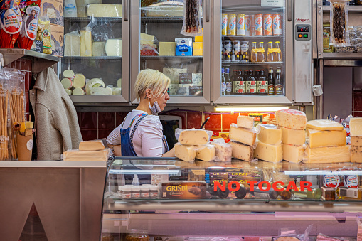 Young female clerk selling cheese in a market stall in the public marketplace Cooperativa Mercado Nuestra Señora De África which is partly under roof and established in 1943 in the center of Santa Cruz which is the main city on the Spanish Canary Island Tenerife