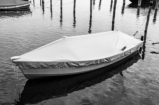Covered and roped boat in the lake water in black and white