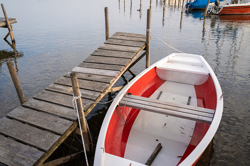 White and red boat roped to the wooden pier in the lake in the morning