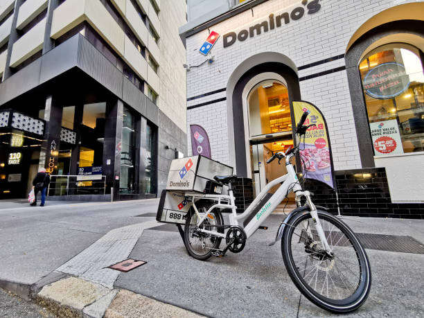 이글 스트리트(eagle street)에 있는 도미노의 피자 지점(domino's pizza branch)은 거리에 배달 자전거 공원이 있습니다. 그 장면에 한 남자가 걷고 있습니다. - dominos pizza 뉴스 사진 이미��지