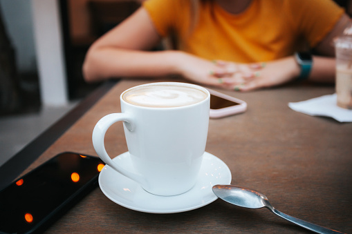 Cup of coffee, on the table in the middle of a conversation between two people.