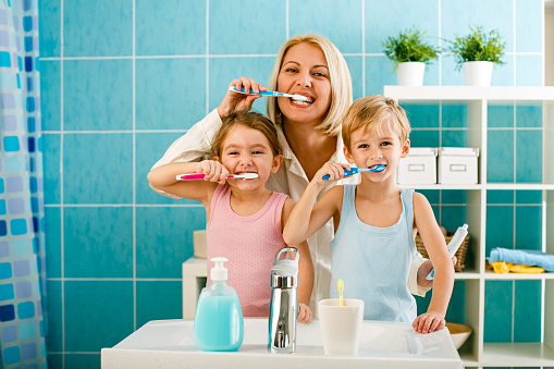 Mother brushing her teeth together with her children in the bathroom