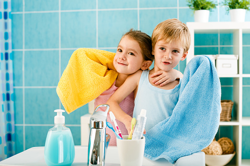 Children looking at the mirror and smiling with their towels, washing faces in the morning as a daily hygiene routine