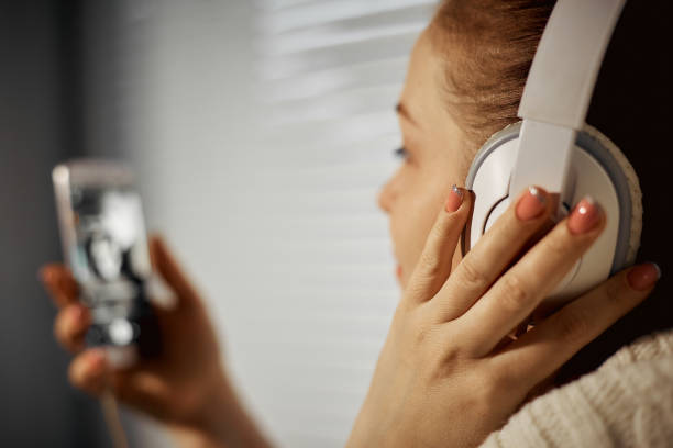 rest and relaxation, young Caucasian woman listening to music in headphones using a smartphone sitting on the windowsill stock photo