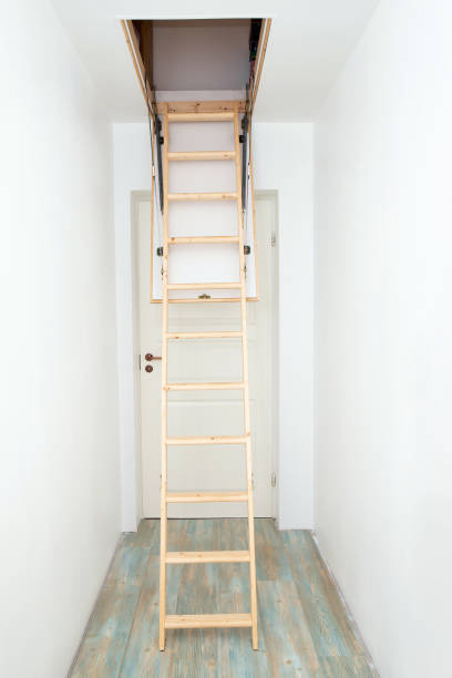 istock Wooden foldable pull up attic stairs ladder at empty white home corridor. Narrow hallway with white walls and blue laminate flooring. 1395380864