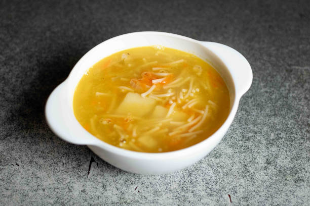 sopa de pollo con fideos, papas, cebollas y zanahorias en un plato blanco profundo sobre un fondo gris. - noodle soup fotografías e imágenes de stock