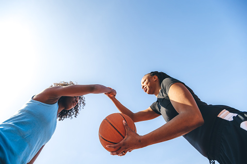 Two young sporty women shaking hands under on basketball court.