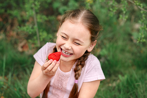 Portrait of Happy cute little girl is eating strawberries at summer day. Soft focused